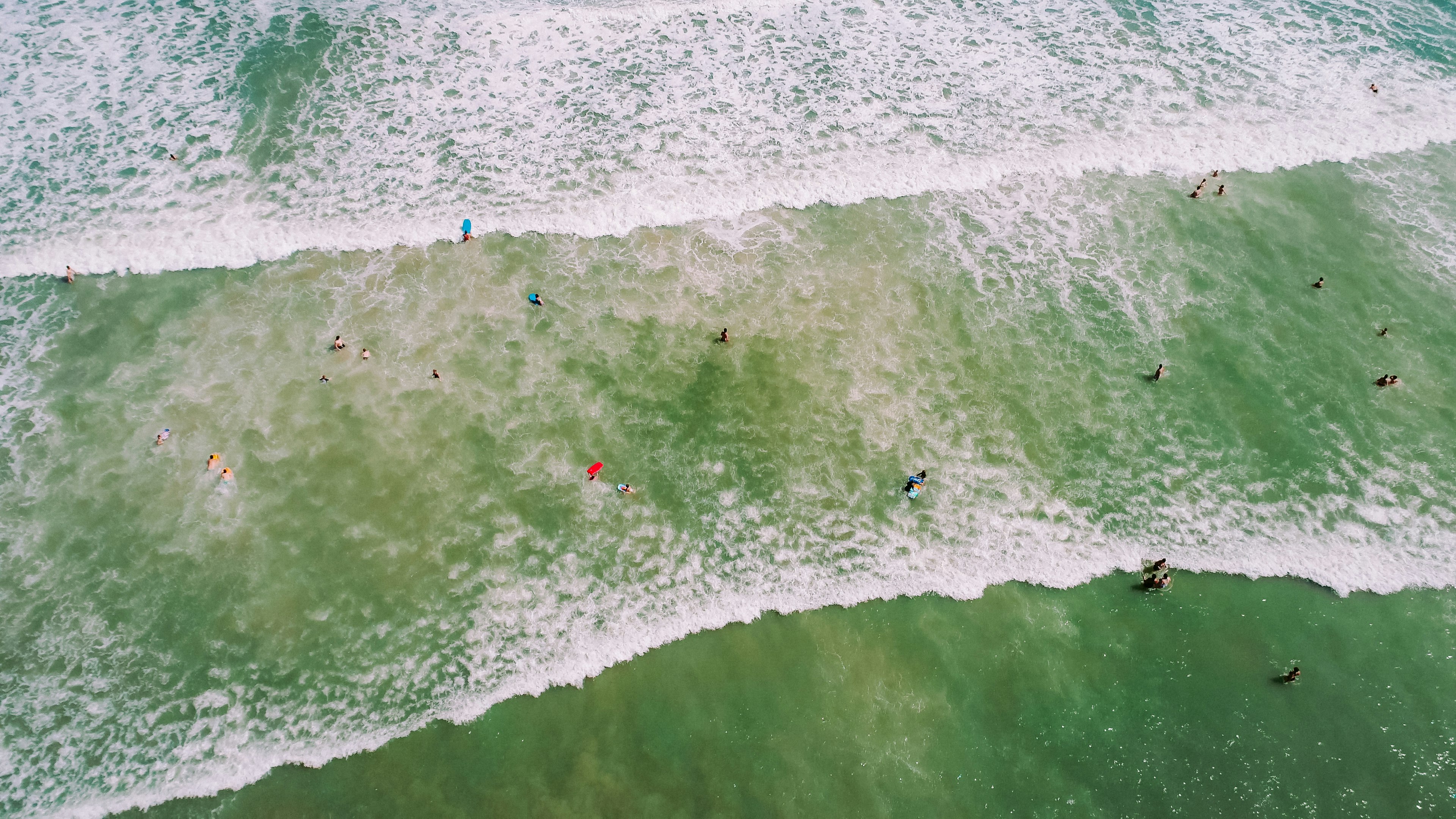 aerial photo of people on seashore with waves and bubbles at daytime